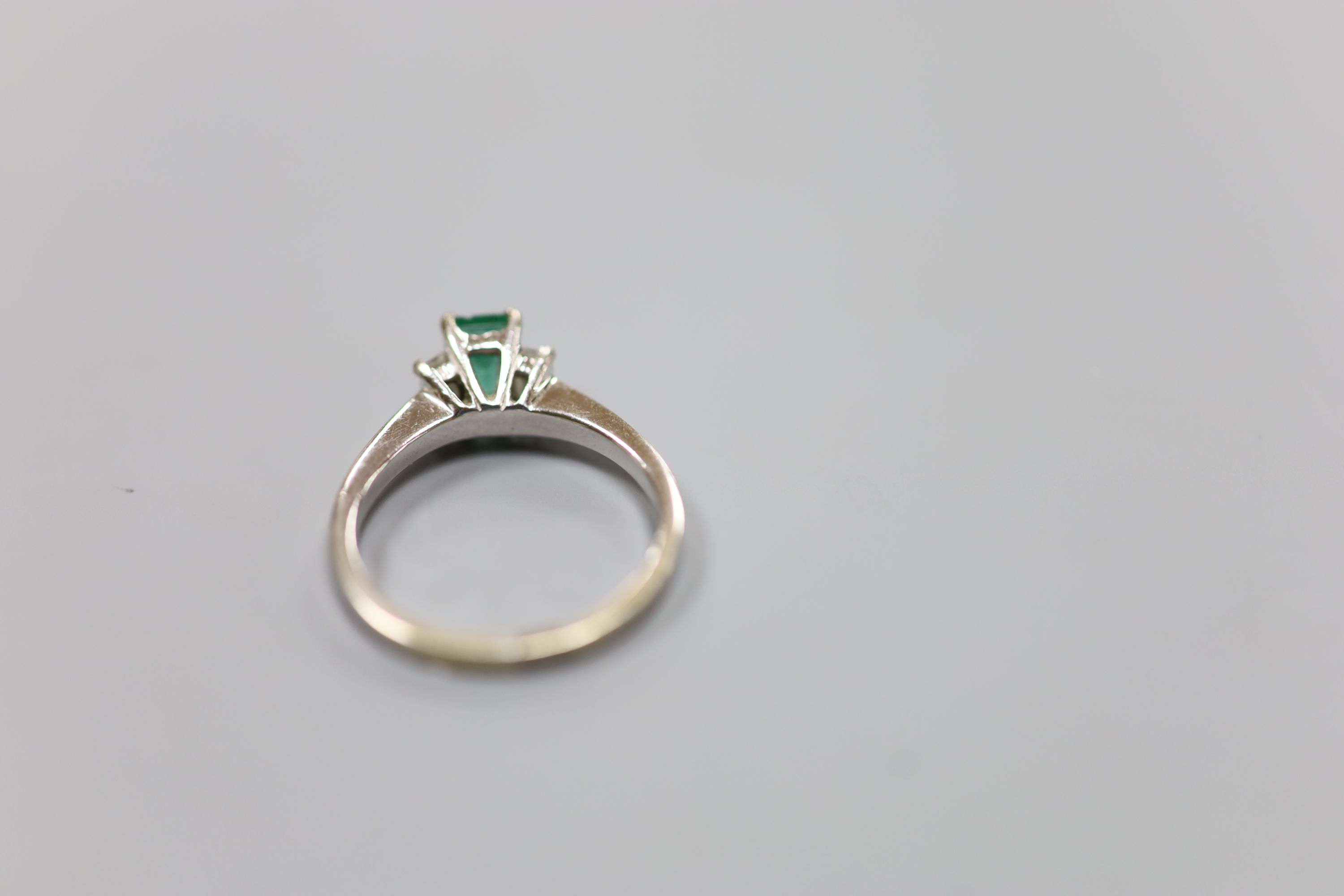 A modern white metal (engraved 750), emerald and diamond set three stone ring, size P